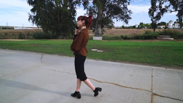 Chica joven paseando por el parque mientras se comunica por una llamada con amigos y familiares.