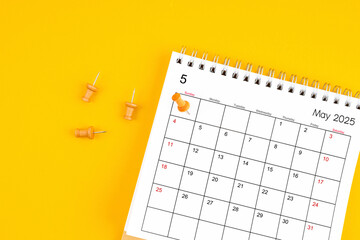 May 2025 Monthly desk calendar for 2025 year with wooden pin on yellow background.