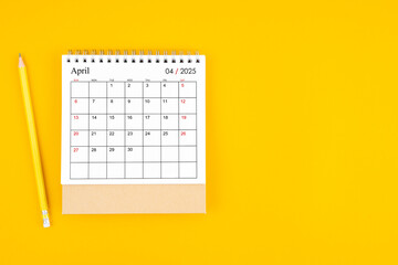 April 2025 desk calendar and wooden pencil on yellow color background.