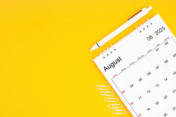 August 2025, Monthly desk calendar for 2025 year and pen with paper clips on yellow color...