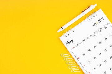 May 2025, Monthly desk calendar for 2025 year and pen with paper clips on yellow color background.