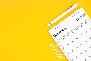 December 2025, Monthly desk calendar for 2025 year and pen with paper clips on yellow color...