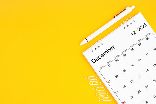 December 2025, Monthly desk calendar for 2025 year and pen with paper clips on yellow color background.