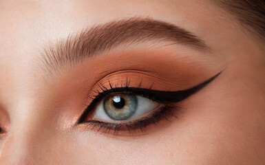 Obraz premium A close-up of a person's eye, emphasizing the eyelashes, eyelid makeup, and the eye itself. The eye has a striking blue hue, and the eyelid is adorned with a warm, peach-colored eyeshadow. 