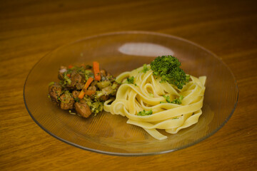 A plate of tagliatelle pasta garnished with fresh broccoli, served alongside stir-fried vegetables and marinated chicken, creating a balanced and colorful meal.