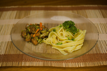 A delightful combination of tagliatelle pasta topped with fresh broccoli and served alongside sautéed vegetables and chicken, presented on a bamboo mat for a rustic touch.