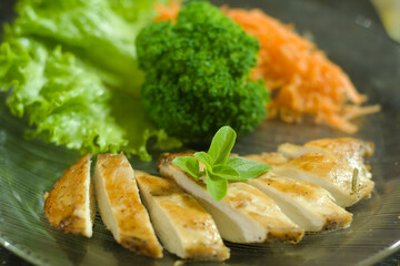 Sliced grilled chicken breast garnished with herbs, served alongside crisp lettuce, steamed broccoli, and shredded carrots on a transparent glass plate.