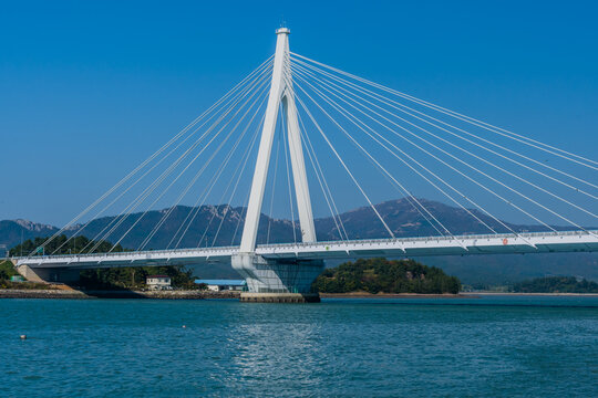 A cable-stayed bridge spanning across a ocean inlet with mountains in the background under a clear blue sky, located in Wando, South Korea
