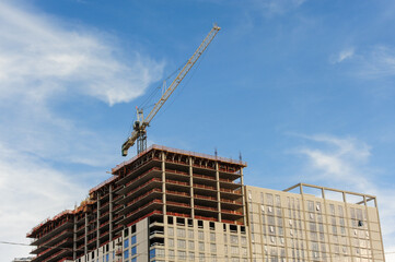 A modern skyscraper under construction with a towering crane, steel framework, and glass facade, set against a vibrant blue sky with scattered white clouds, showcasing urban development progress
