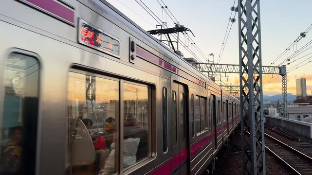A modern commuter train travels on elevated tracks at sunset with city buildings in the distance