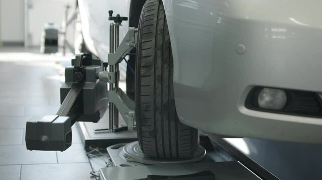Mechanic performing a wheel alignment process in a modern workshop. Professional equipment is used to ensure accurate vehicle alignment for optimal performance and safety