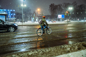 Cyclist navigates through vehicle traffic during heavy snowfall, pedaling over slushy uncleared...