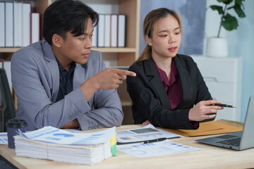 Business partners working together on a new project, analyzing financial documents using a calculator in a meeting. Talking at the desk Analyze data from graphs and charts to solve business problems.