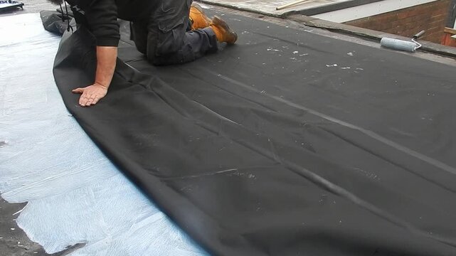 Man covering flat roof rolling rubber waterproof sheet to prevent leaking surface