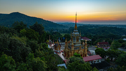 Fototapeta premium Aerial view of Mae Klang Waterfall Temple in Chiang Mai with the sunrise casting warm hues in calm sky. The tranquil setting highlights the serene beauty of the temple and the natural landscape.