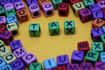 Colorful Alphabet Blocks Spelling 'Tax' on Yellow Background Surrounded by Letters