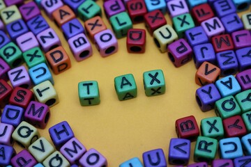 Colorful Alphabet Blocks Spelling 'Tax' on Yellow Background Surrounded by Letters