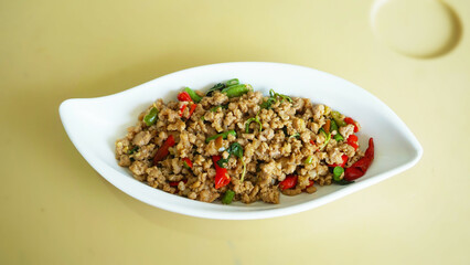 Authentic Thai Basil Pork, Pad kra pao Thai cuisine is a spicy and savory stir-fry dish featuring ground meat and holy basil in White Boat Shaped Dish.	