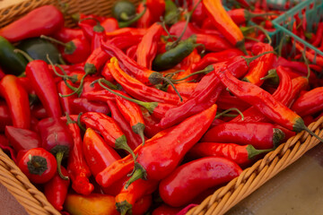 A view of a basket full of a variety of red chili peppers, on display at a local farmers market.