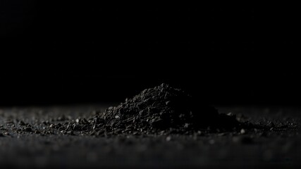Dark pile of fine granular material against black background