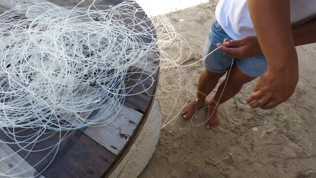 Hands are shown skillfully working to untangle a mess of fishing line with hooks, ensuring the line is ready for fishing. The activity takes place at a dock surrounded by natural scenery.