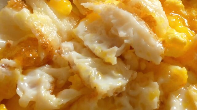 A close up shot of scrambled eggs after being cut up with fork and knife.
