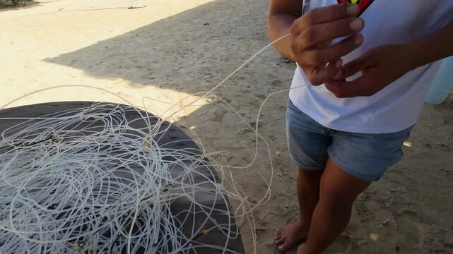 A fisherman skillfully untangles a mix of fishing lines and hooks while standing on the sandy beach. The sun shines brightly, creating a perfect backdrop for this relaxing afternoon activity.