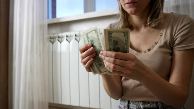 Woman counts dollars near a heater, expressing concern over rising energy costs and increasing utility bills. Financial stress related to home heating becomes evident