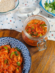 A close-up view of a glass jar filled with vibrant homemade kimchi, showcasing its fermented texture and the addition of green onions and red pepper flakes.