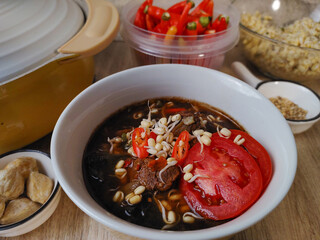  A bowl of Rawon, an Indonesian beef stew with a deep, dark broth, topped with bean sprouts, tomatoes, and chili peppers. Rawon, a Rich and Savory Indonesian Beef Stew