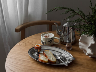 Delicious breakfast - boiled egg, cappuccino bun with butter on a round wooden table