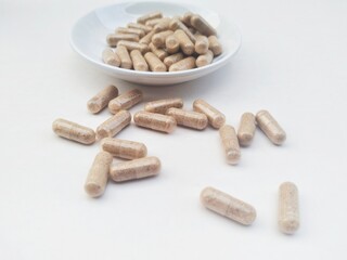 High angle view of capsule pills in a small white plate on a white background. 