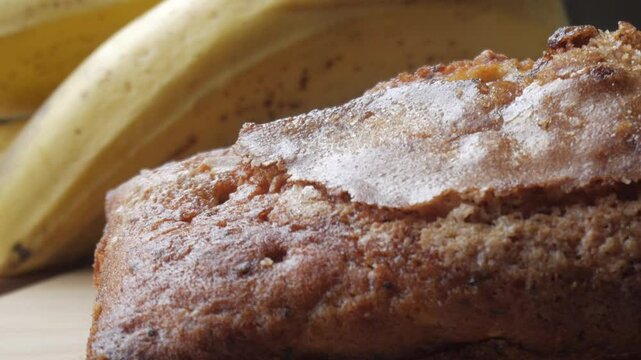 Right pan view of banana bread cut in half on a wooden board with a bananas in the back.