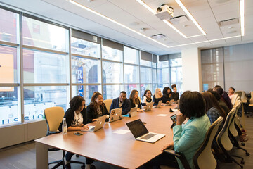 A modern meeting room with a long wooden table, ergonomic chairs, and large windows providing...