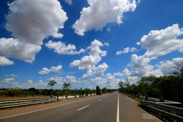 A long road under a blue sky with fluffy clouds