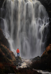 person standing at a waterfall Known as Clashnessie falls located on the NC500 route in North west Scotland.