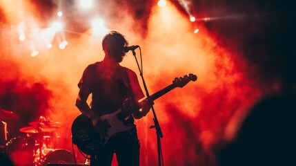 Silhouette of guitarist performing on stage in dramatic red lighting.