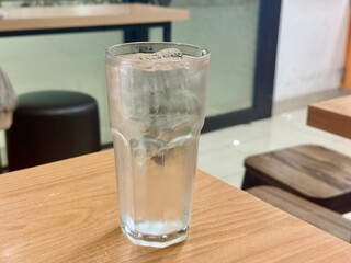Glass of water with ice cube, placed on rustic wooden table.