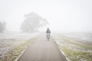Cold misty day in the Netherlands. Lady cycles on Dutch cyclepath in Hoge Veluwe heavy fog that limits visibility. Bad weather brings transport danger