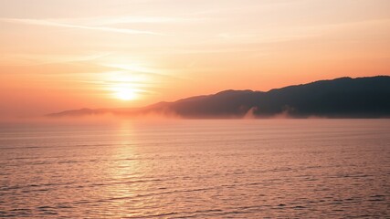 Fototapeta premium Serene Sunrise Over Misty Coastal Mountains and Calm Water