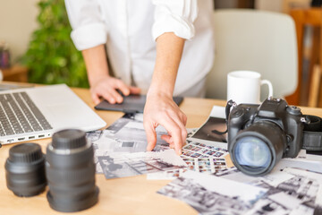 Photographer selecting images from contact sheet in bright office with laptop, camera, and lenses