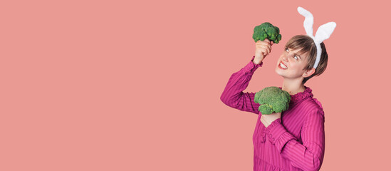 Studio shot of a young Caucasian woman in bunny ears holding organic and fresh broccoli in her hands. healthy eating.A panoramic banner with a copy of space.