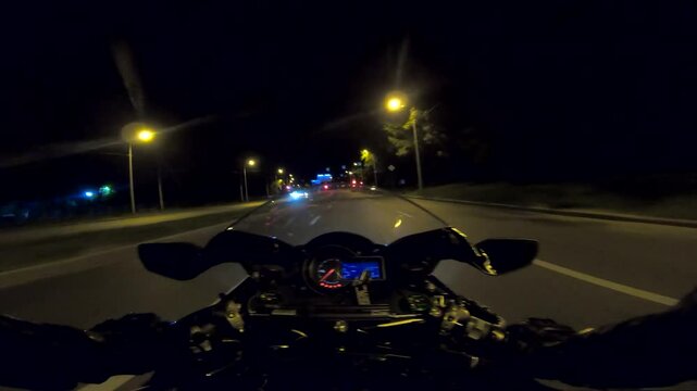The viewpoint of motorcycle rider driving on motorbike at evening urban road on high speed. Male motorcyclist riding on modern sport bike in the illuminated city streets at night. Freedom concept. POV