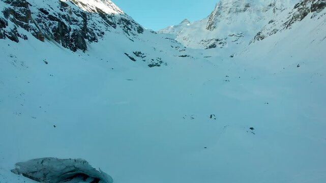 Aerial view of a remote snow covered mountain valley of the Swiss Alps with hikers walking towards giant glacier cave in Valais, Switzerland during a cold winter day as the sun starts to set