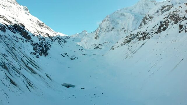 Aerial flyover over a remote snow covered mountain valley of the Swiss Alps with a giant glacier cave in Valais, Switzerland during a cold winter day as the sun starts to set