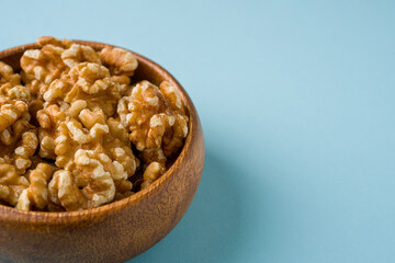 Top view of heap of walnut kernels in wooden bowl on blue background