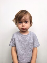 Naklejka premium A cute little boy with a surprised face and disheveled hair. The emotion of surprise in a child. Close-up of a beautiful child with a surprised look on a white background