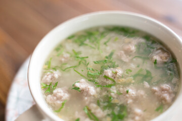 A bowl of rice soup with minced pork and herbs.