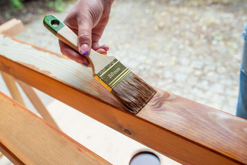 Close-up of a worker’s hand applying wood stain with a paintbrush on wooden beams during a DIY...