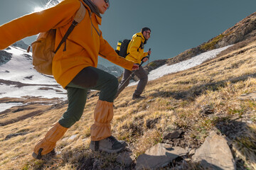 Travelers go uphill with backpacks and trekking poles, a side view of the background with snowy...